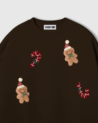 Close-up of hand-stitched plush gingerbread men and candy canes on dark brown heavyweight cotton fleece showing 3D texture