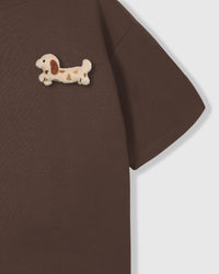 Close-up of spotted dachshund plush on shoulder area of brown tee showing plush detail