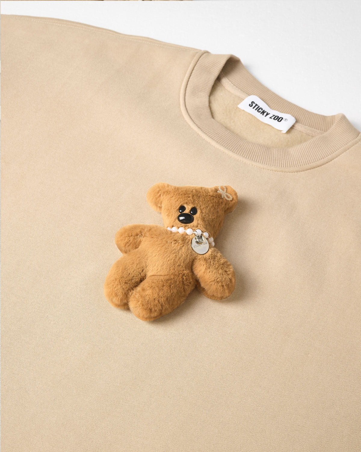 Detail of hand-stitched teddy bear applique on STICKYZOO cream sweatshirt showing dimensional craft