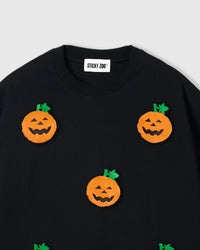 Close-up of plush pumpkin applique showing orange body, carved face, and green stem detail