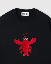 Close-up of plush shrimp on black cotton showing red body, googly eyes, and claw detail