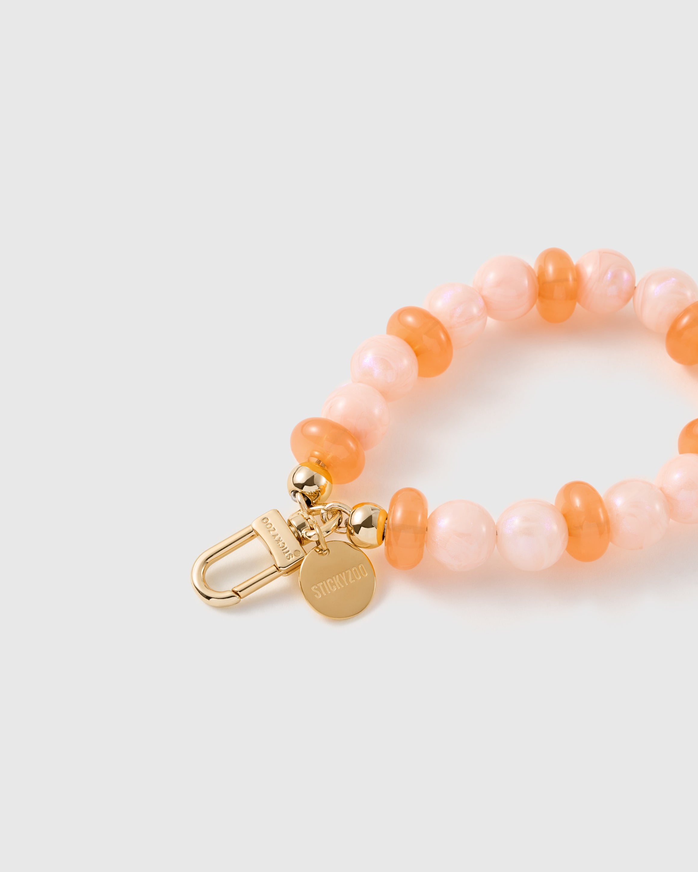 Close-up of the 18K gold-plated hook, engraved STICKYZOO disc and pearly peach beads — no two alike