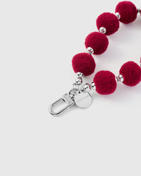 Crimson plush phone strap hanging from phone showing hands-free wrist carry
