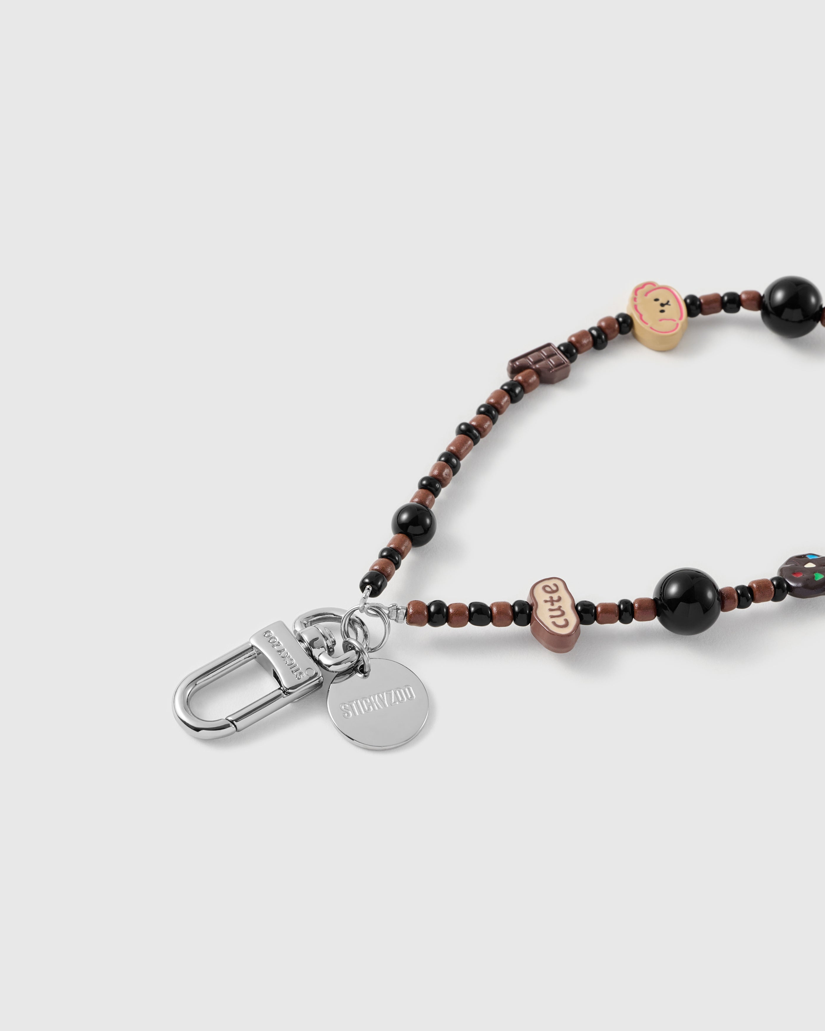 Close-up of the silver-tone hook, engraved STICKYZOO disc and the football, chocolate and puppy charms — each strap strung by hand