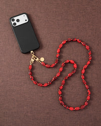 Ruby smoke link phone strap attached to phone on dark brown fabric lifestyle flat-lay