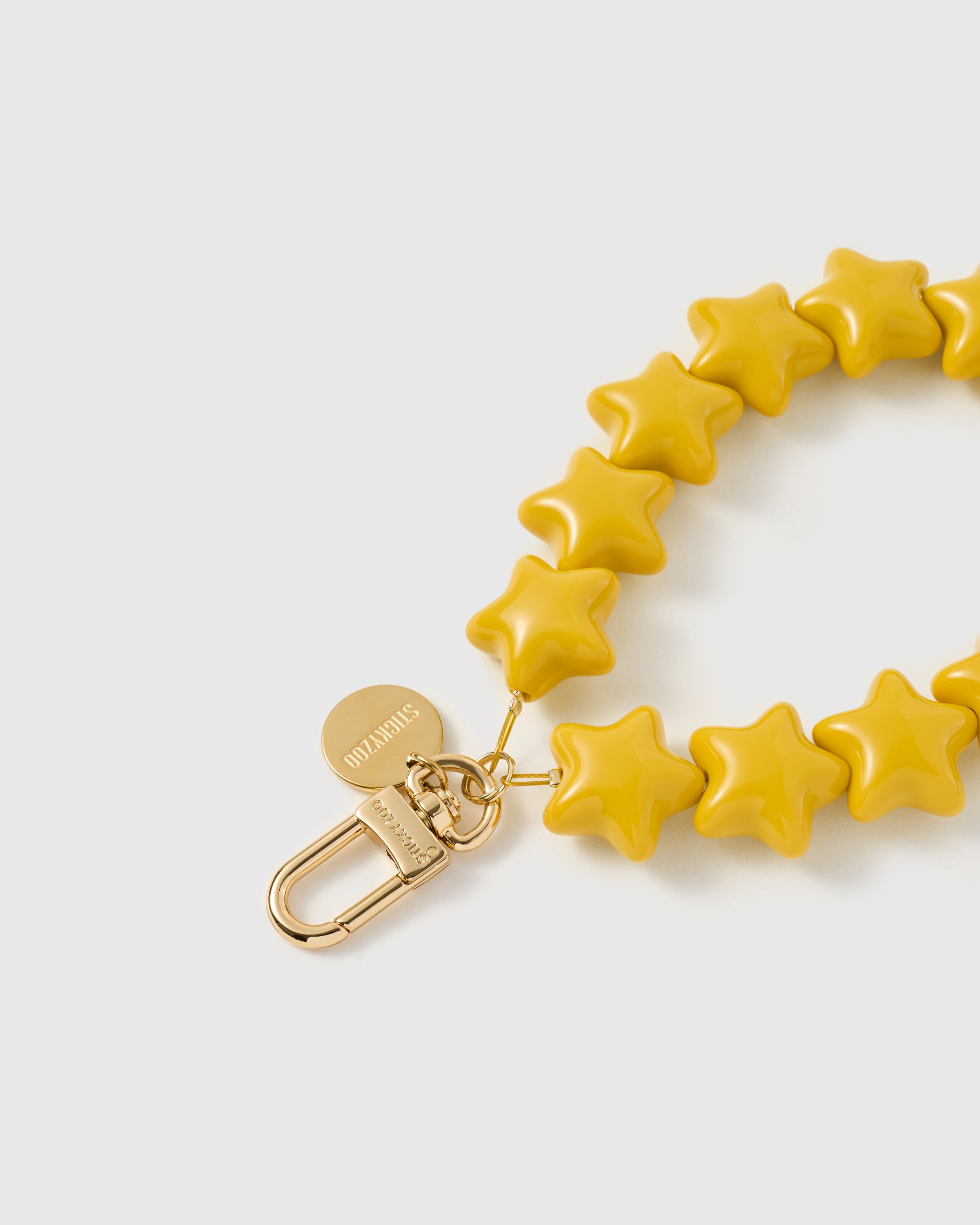 Close-up of 18K gold-plated carabiner and engraved STICKYZOO disc on honey-gold star bead strand