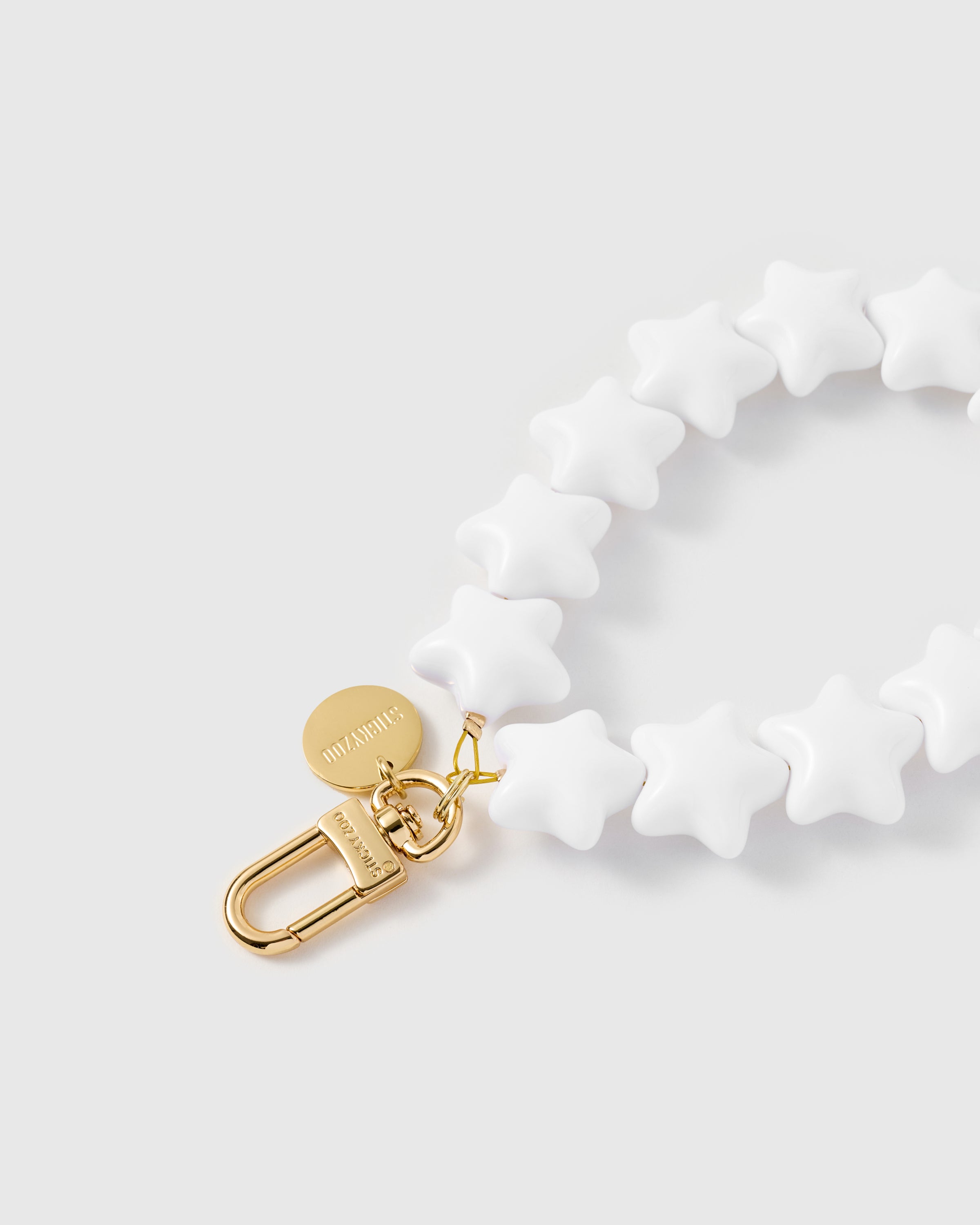 Close-up of 18K gold-plated carabiner and engraved STICKYZOO disc against glossy ivory star beads — Rated 4.9 stars