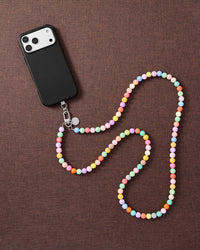 Full-length pastel cross-body phone strap draped beside a phone on linen, worn hands-free across the body.