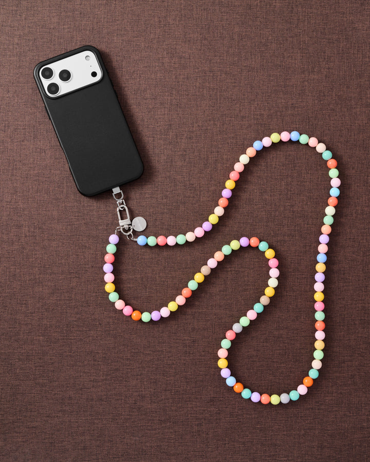 Full-length pastel cross-body phone strap draped beside a phone on linen, worn hands-free across the body.