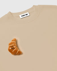 Detail of rolled plush croissant near hem on cream base showing layered dimensional construction