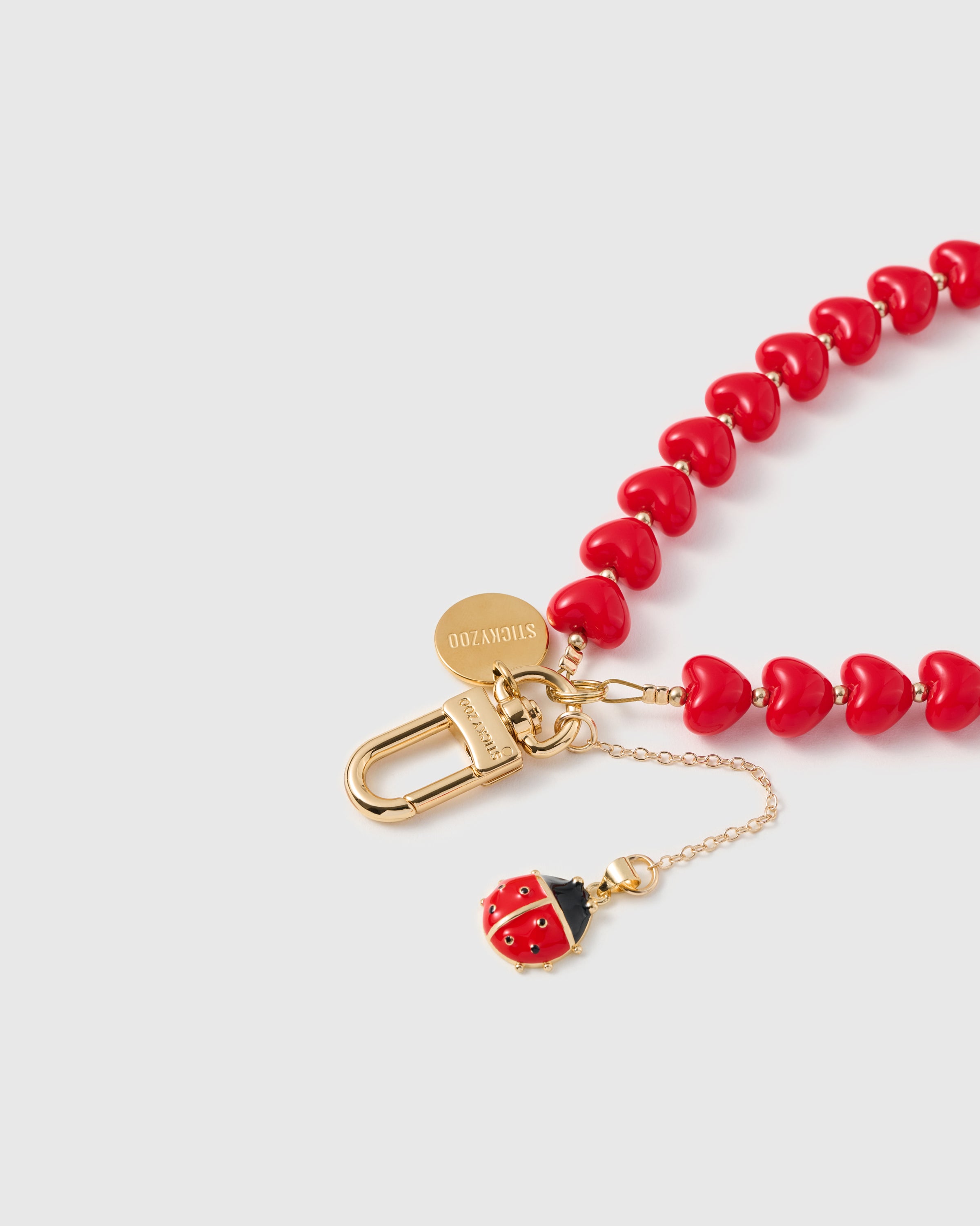 Close-up of 18K gold-plated carabiner and engraved STICKYZOO disc on crimson heart strand