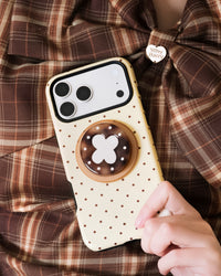 Hand holding the lucky clover phone case with the tortoiseshell MagSafe grip extended from the back