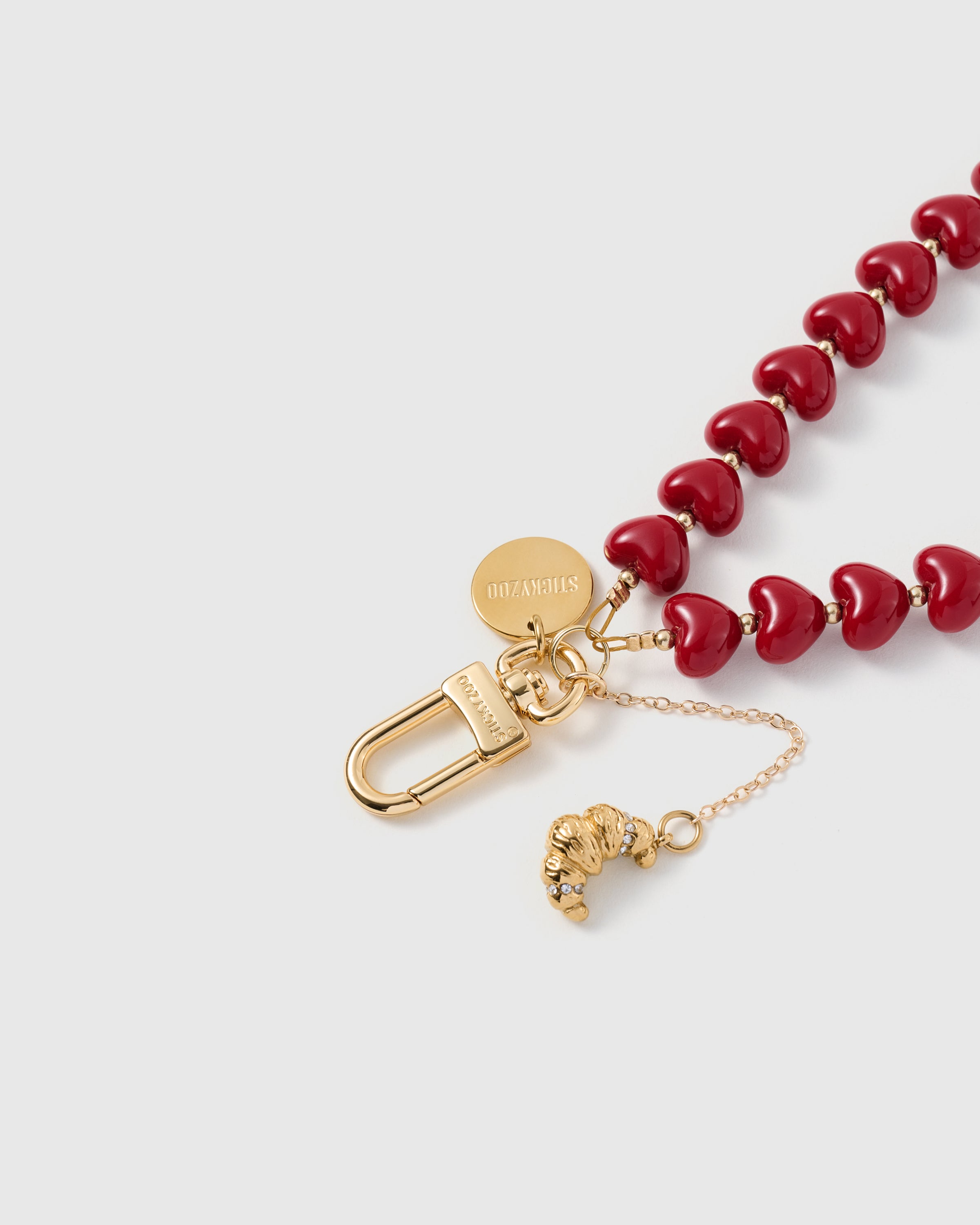Close-up of 18K gold-plated carabiner and engraved STICKYZOO disc on cherry heart bead strand