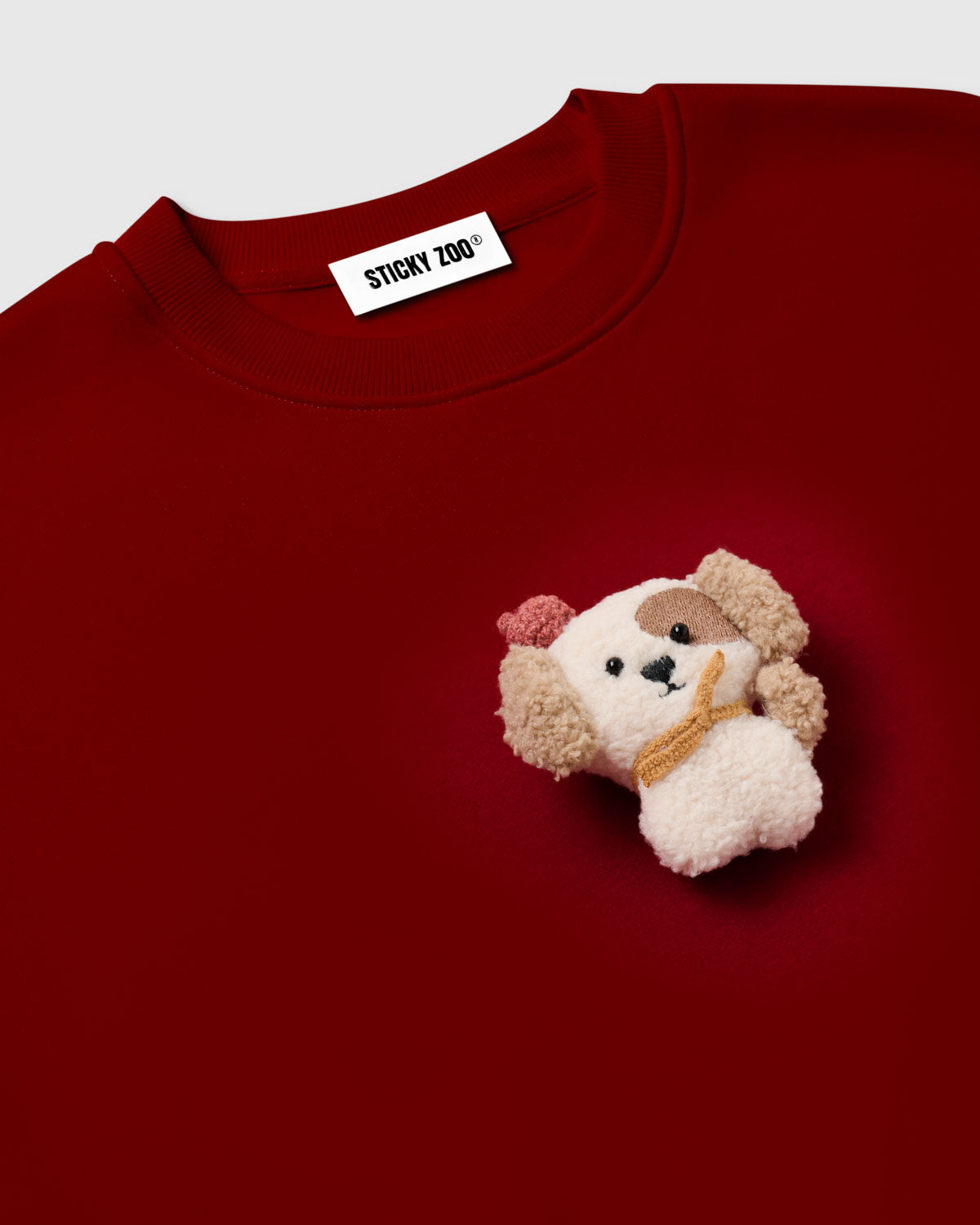 Close-up of 3D plush puppy with brown eye patch and floppy tan ears on STICKYZOO red sweatshirt