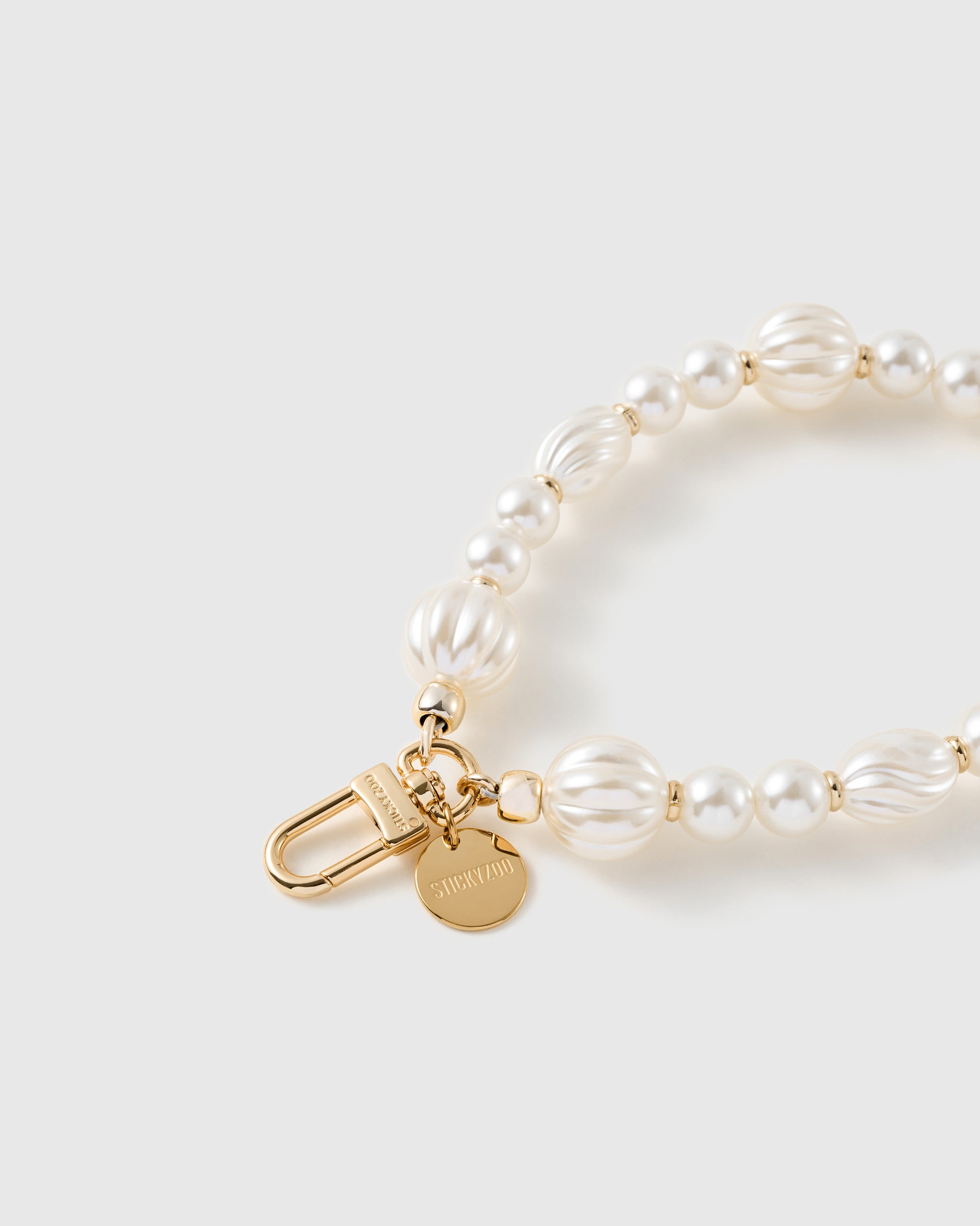 Macro of the 18K gold-plated clasp and engraved STICKYZOO charm disc on the pearl-style beaded strap