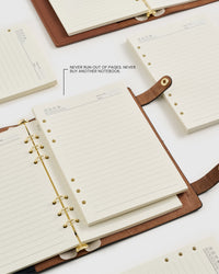 Several A5 refill packs and ring notebooks laid out together — premium lined paper made for long-term daily use.