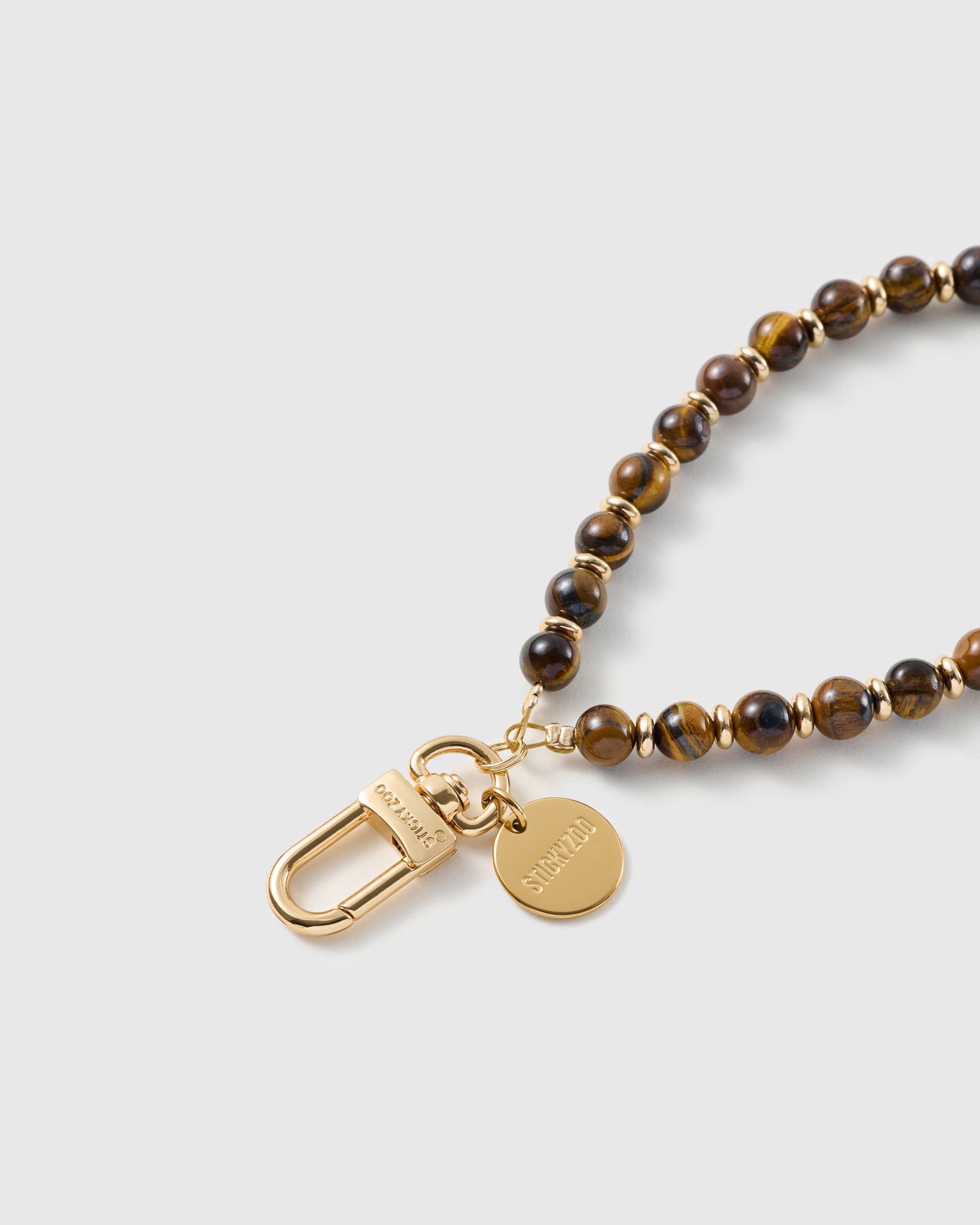 Macro of the 18K gold-plated hook and engraved STICKYZOO charm disc on the bronze stone strap