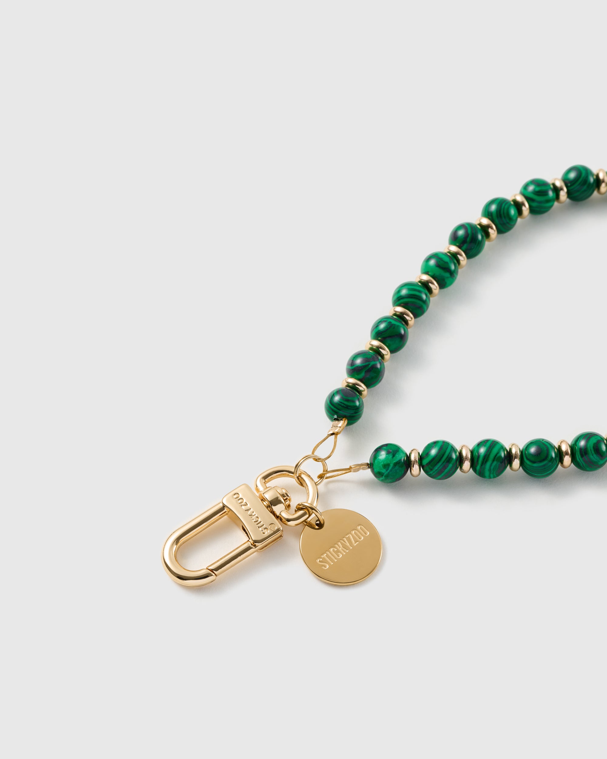 Macro of the 18K gold-plated clasp and engraved STICKYZOO charm disc on the deep green beaded strap