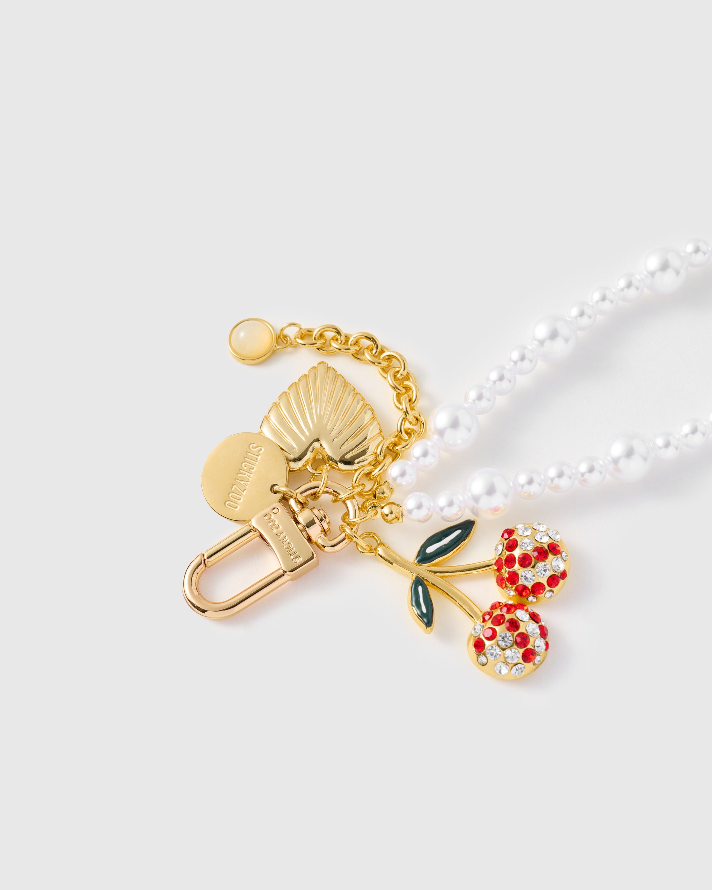 {{18K gold engraved hook}} Close-up of gold-plated STICKYZOO clasp with rhinestone cherry charm, shell-heart, and pearl beads