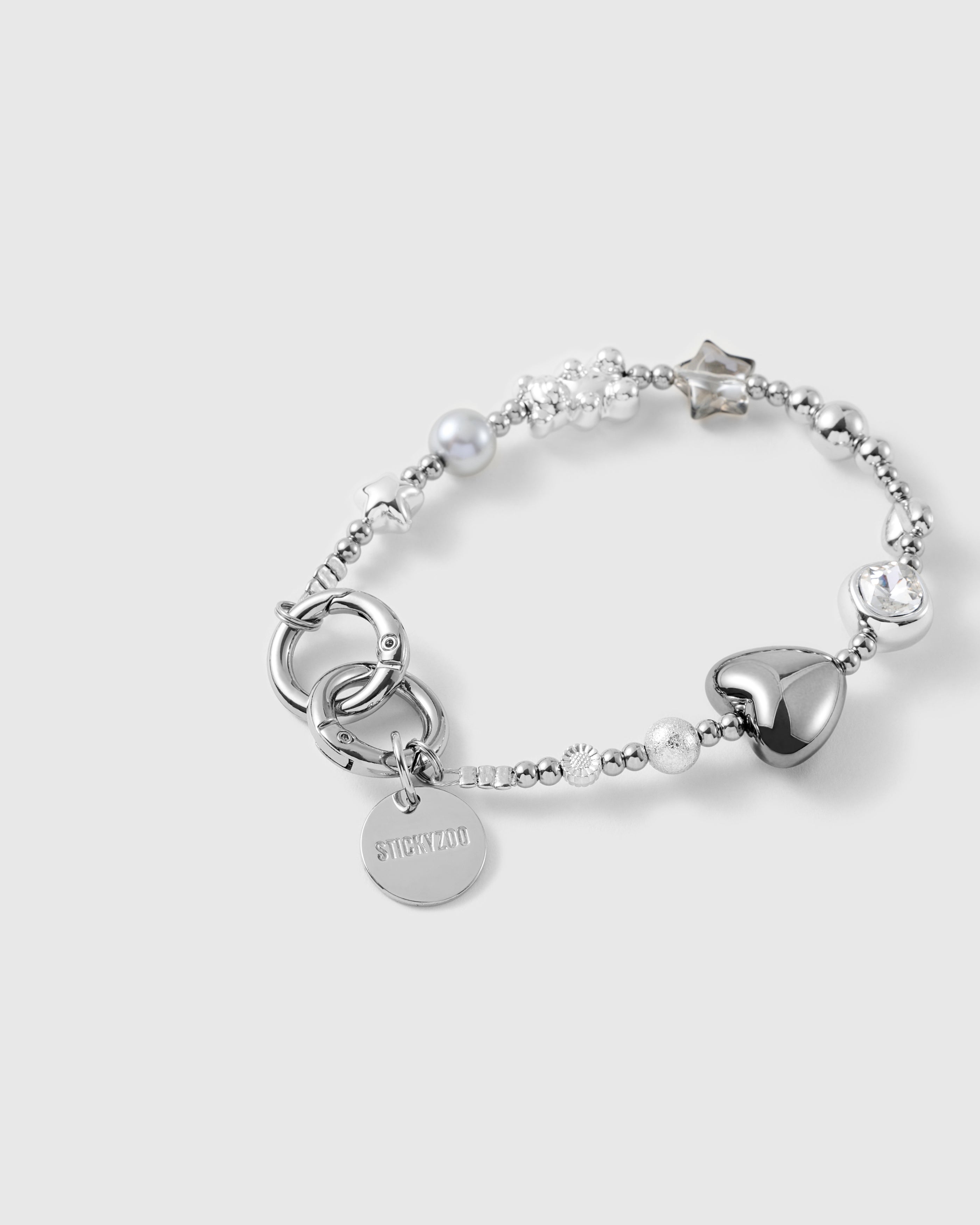 Close-up of the glossy silver puff heart, bezel-set faceted clear bead, grey pearl-effect bead and stardust silver bead with engraved STICKYZOO disc