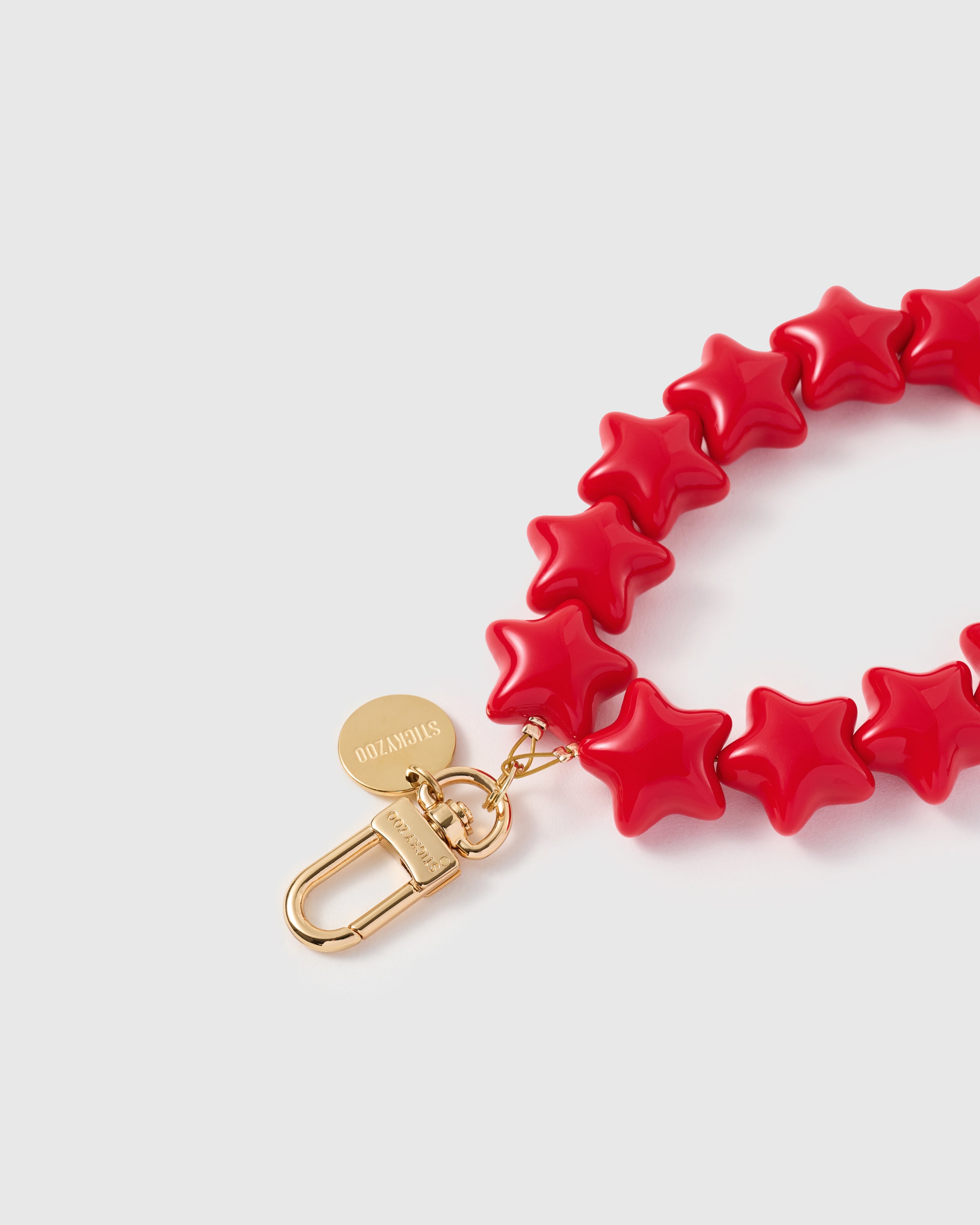 Close-up of 18K gold-plated carabiner and engraved STICKYZOO disc on crimson star bead strand
