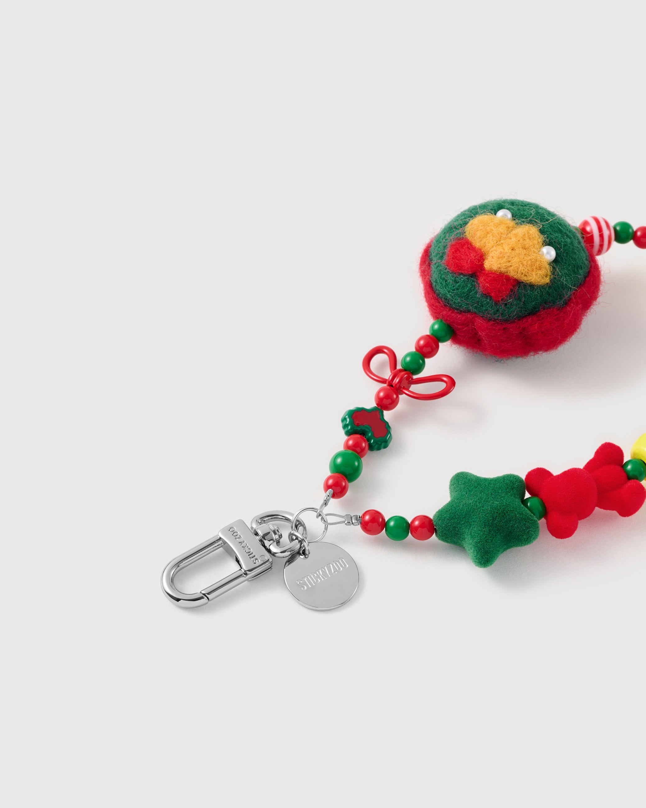 Close-up of the silver-tone hook, engraved STICKYZOO disc and the felted wreath charm with golden bells, flocked star and glossy holiday beads — soft and tactile