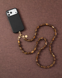 Amber smoke link phone strap attached to phone on dark brown fabric lifestyle flat-lay
