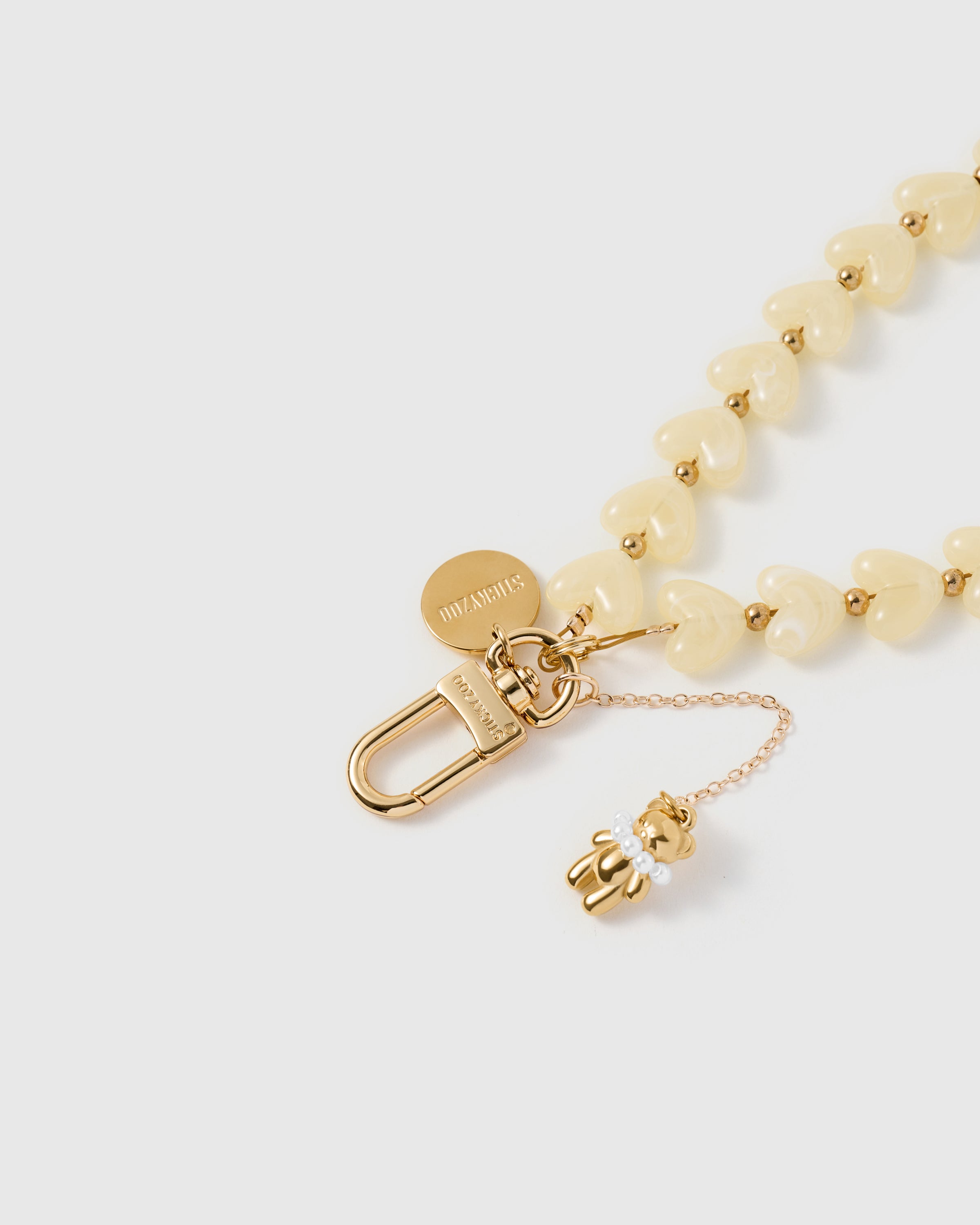 Close-up of the gold-plated carabiner and engraved STICKYZOO disc on the ivory teddy heart phone strap. Loved by Thousands.