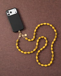 Golden smoke link phone strap attached to phone on dark brown fabric lifestyle flat-lay