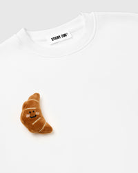 Detail of rolled plush croissant near hem on white base showing hand-stitched dimensional depth