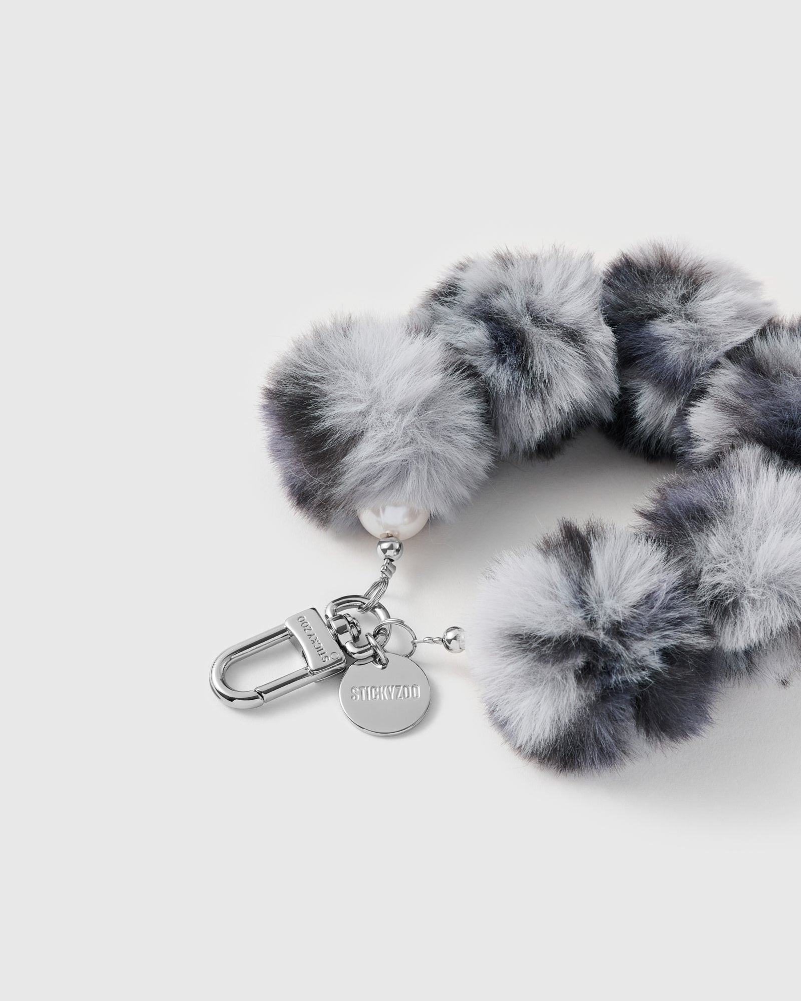 Close-up of the silver-tone hook, engraved STICKYZOO disc and the plush marbled smoke-grey faux-fur poms and pearly accent bead — soft and tactile