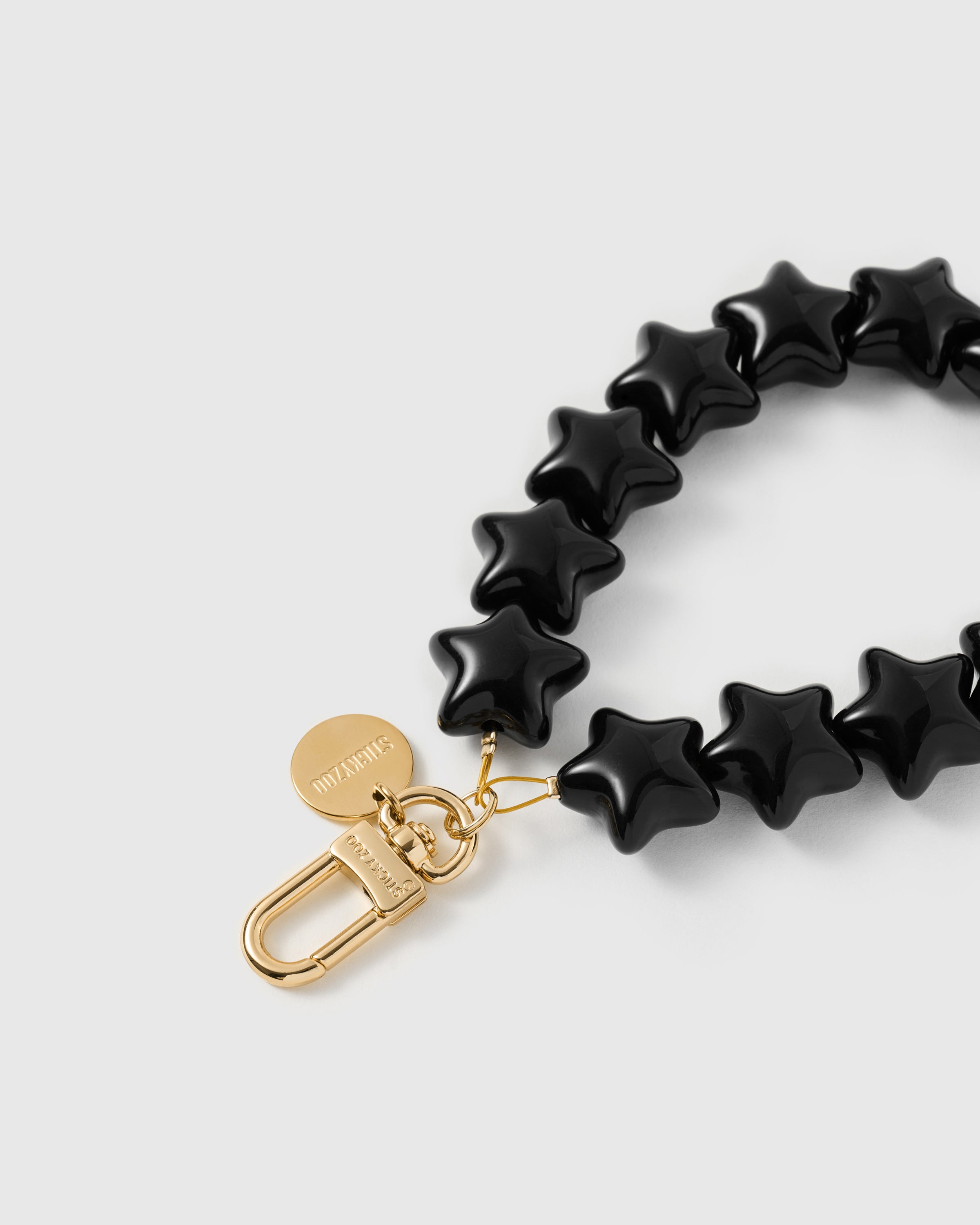 Close-up of 18K gold-plated carabiner and engraved STICKYZOO disc on noir star bead strand