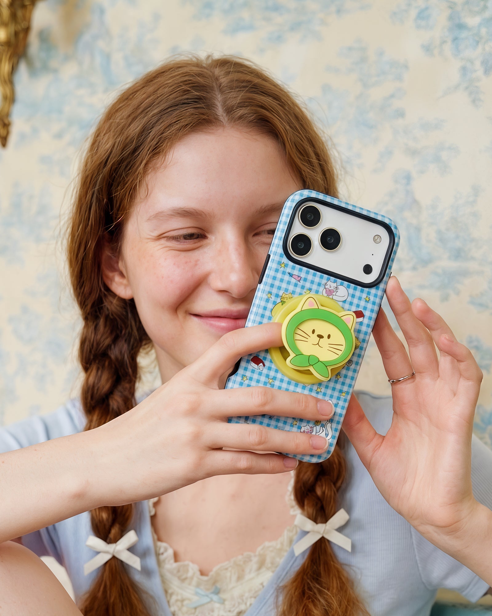 Person holding the STICKYZOO blue hooded-cat phone case with the grip popped out for an easy one-hand hold.