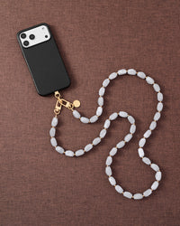 Cloud marble link phone strap attached to phone on dark brown fabric lifestyle flat-lay