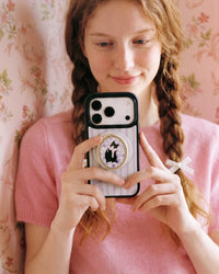Fingers gripping the popped-out retractable MagSafe pop-grip on the back of the tuxedo cat phone case
