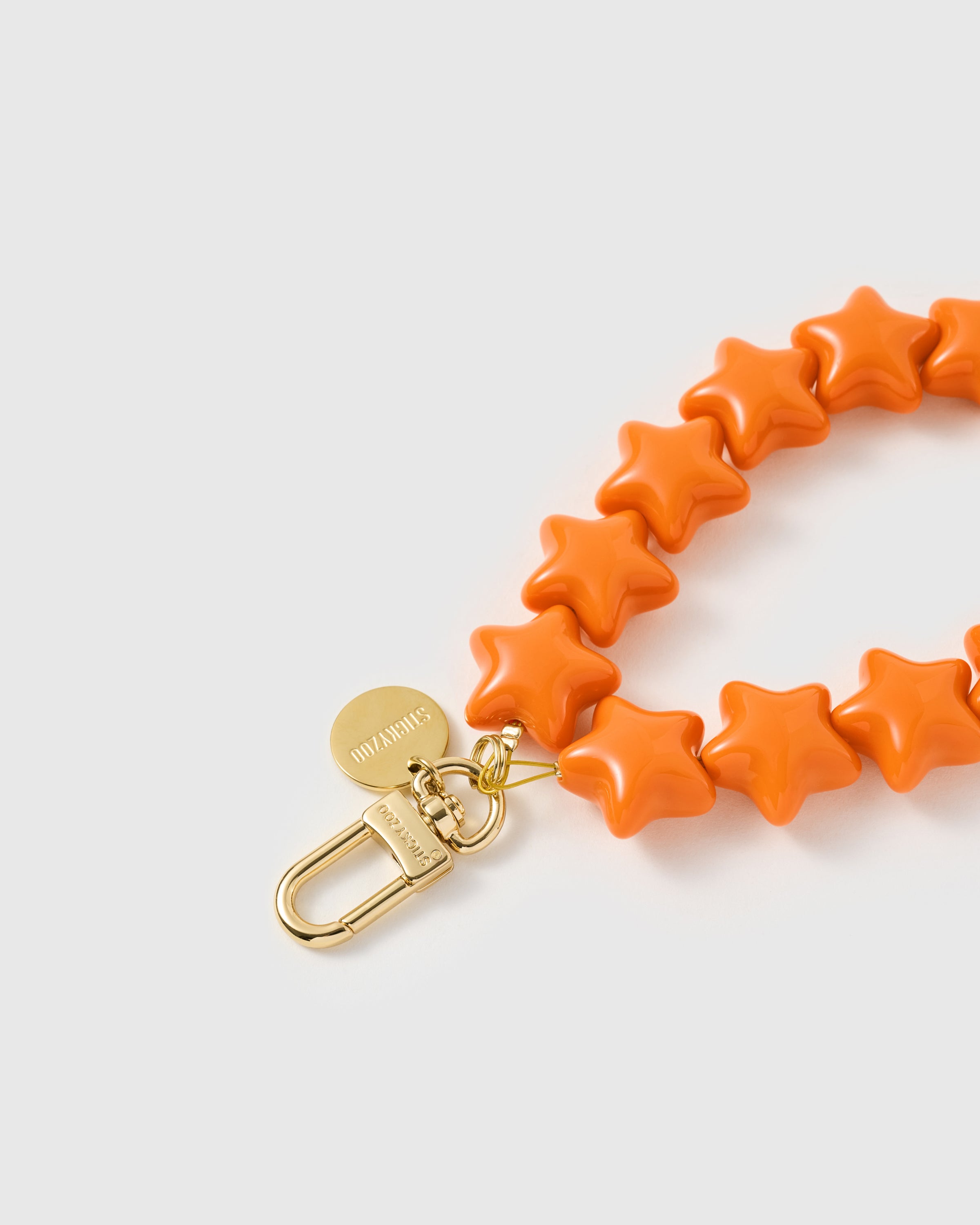 Close-up of the gold-plated carabiner and engraved STICKYZOO disc on the tangerine star phone strap. Loved by Thousands.