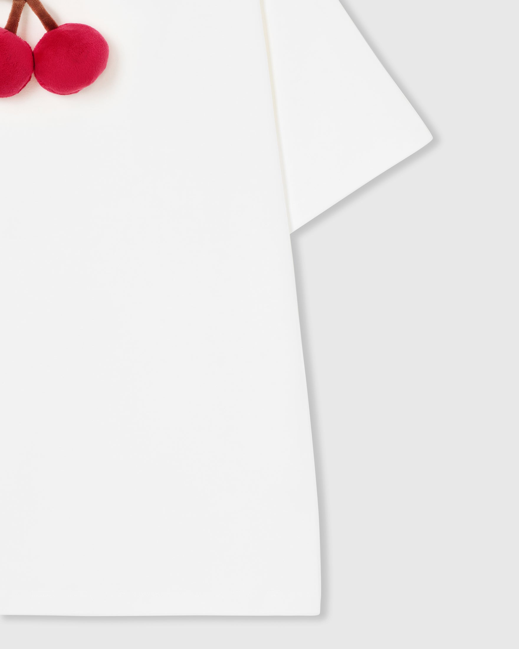 Close-up of hem and side construction on white Cherry T-Shirt with plush cherry detail above