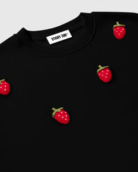 Angled close-up of neckline and chest area showing scattered plush strawberries with brand label visible