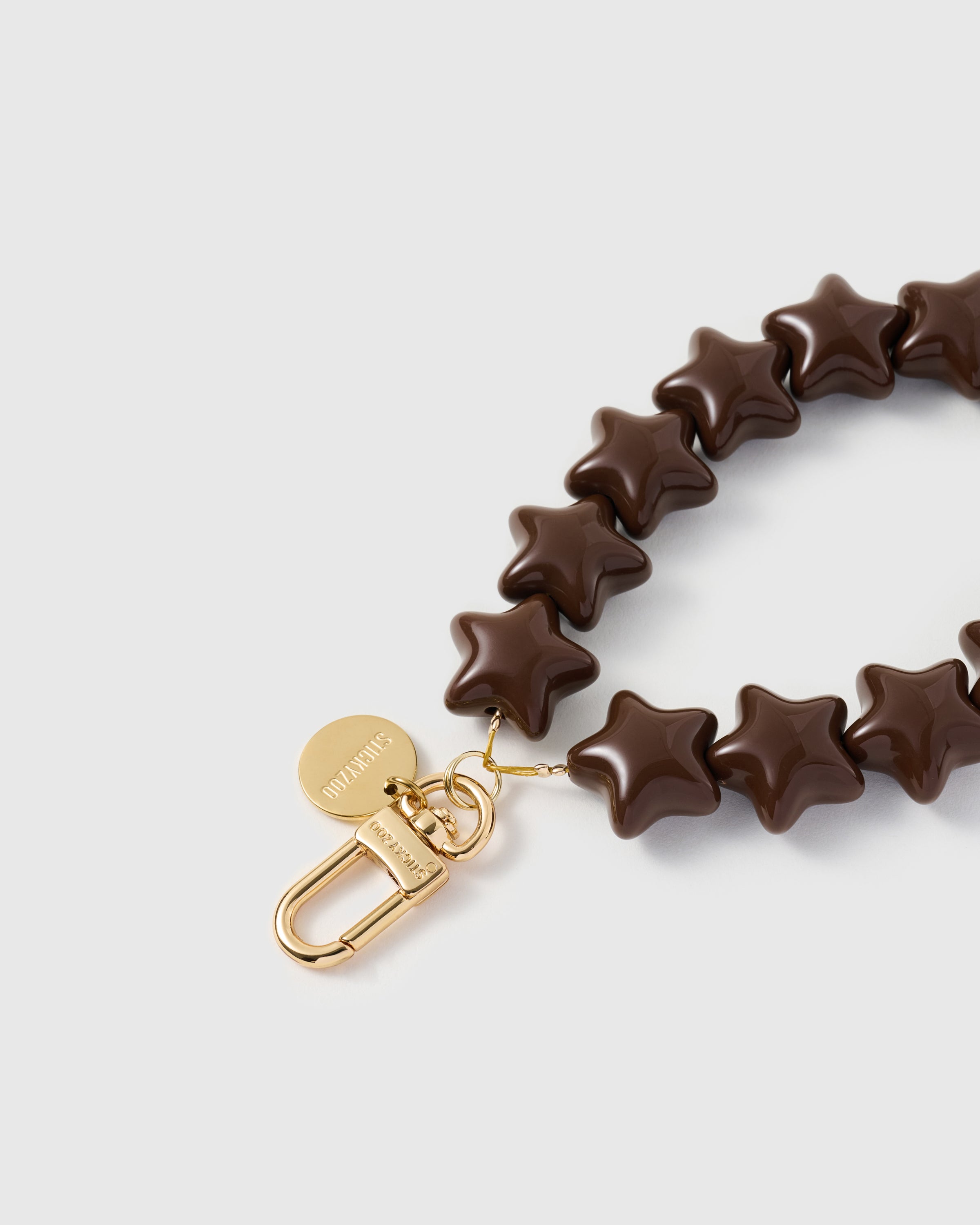 Engraved STICKYZOO — close-up of gold-plated carabiner, engraved disc, and glossy molded resin star beads in cocoa