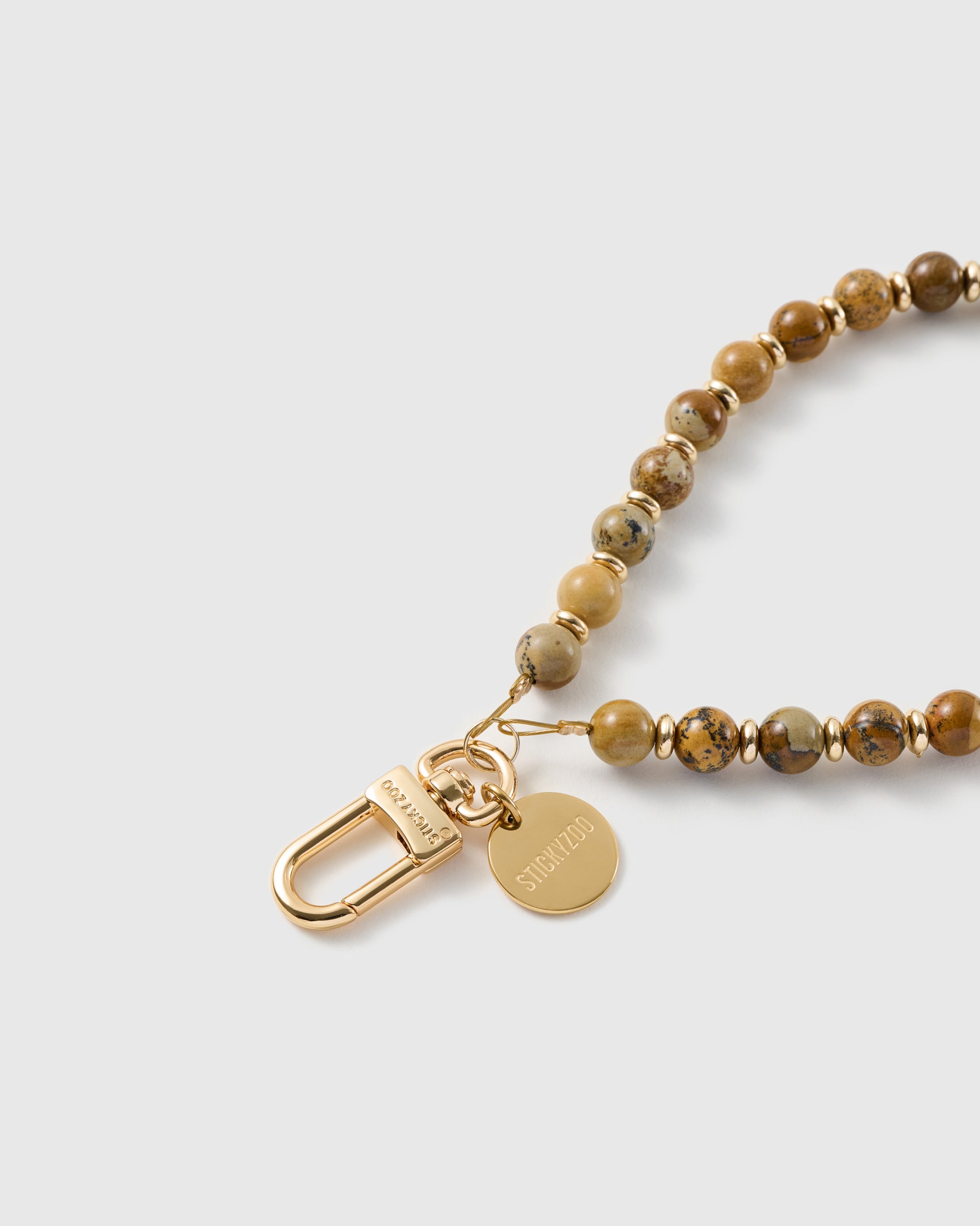 Macro of the 18K gold-plated hook and engraved STICKYZOO charm disc on the handmade stone bead wrist strap.