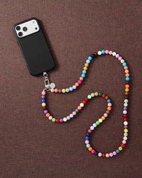 Full-length rainbow cross-body phone strap draped beside a phone on linen, worn hands-free across the body.