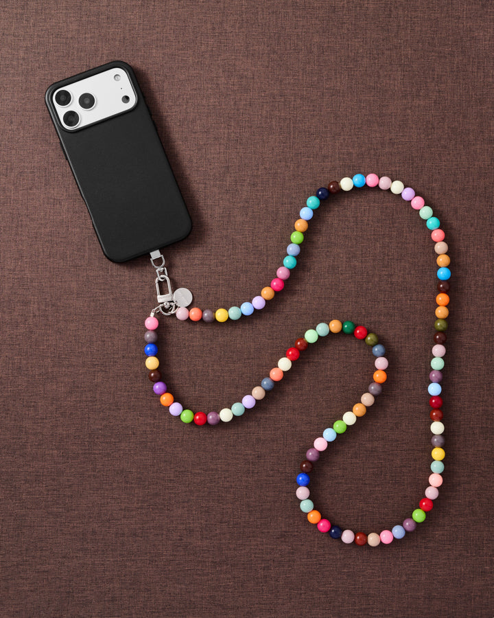 Full-length rainbow cross-body phone strap draped beside a phone on linen, worn hands-free across the body.