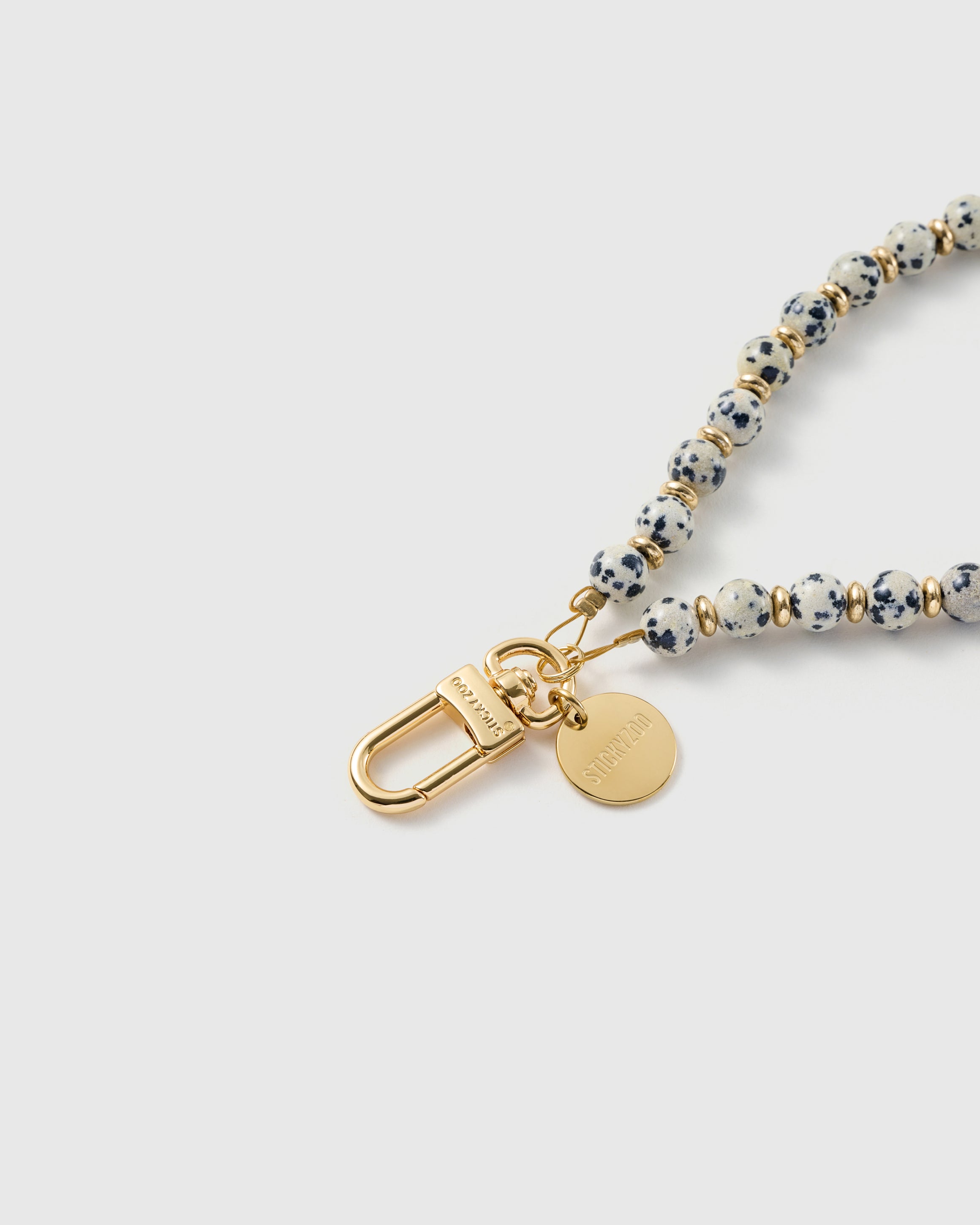 Close-up of the 18K gold-plated hook, engraved STICKYZOO disc and cream speckled stone beads — each one unique