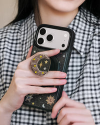 Phone held with fingers around the popped-out beaded moon MagSafe grip on the back of the case