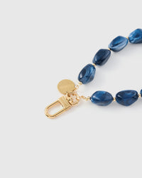 Close-up of gold-plated engraved hook and STICKYZOO charm disc with indigo stone beads