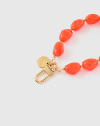 Close-up of gold-plated clasp and engraved STICKYZOO charm disc with vivid coral agate beads