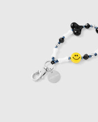 Close-up of glossy red heart charm and yellow smiley bead against black tube beads