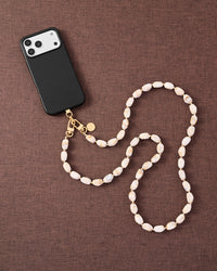 Blush marble link phone strap attached to phone on dark brown fabric lifestyle flat-lay