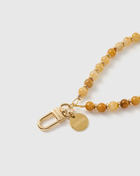 Macro close-up of the 18K gold-plated clasp and engraved STICKYZOO charm disc on the honey-toned stone bead strap