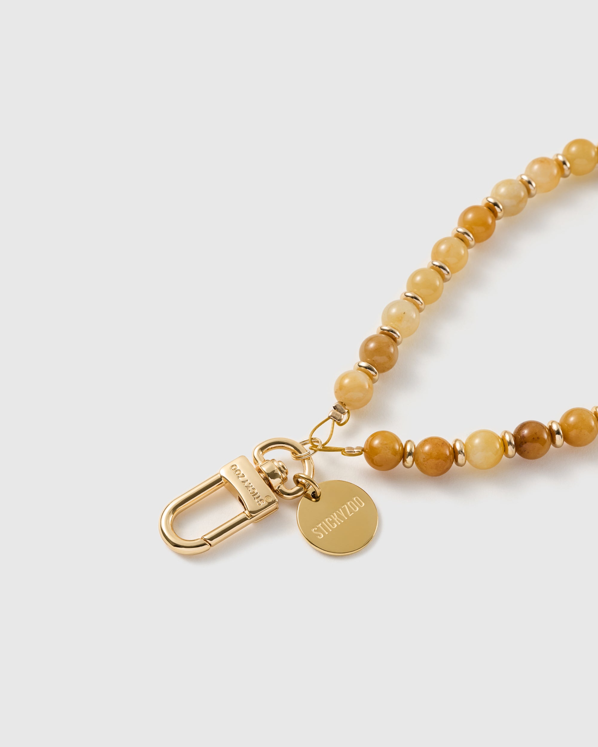 Macro close-up of the 18K gold-plated clasp and engraved STICKYZOO charm disc on the honey-toned stone bead strap